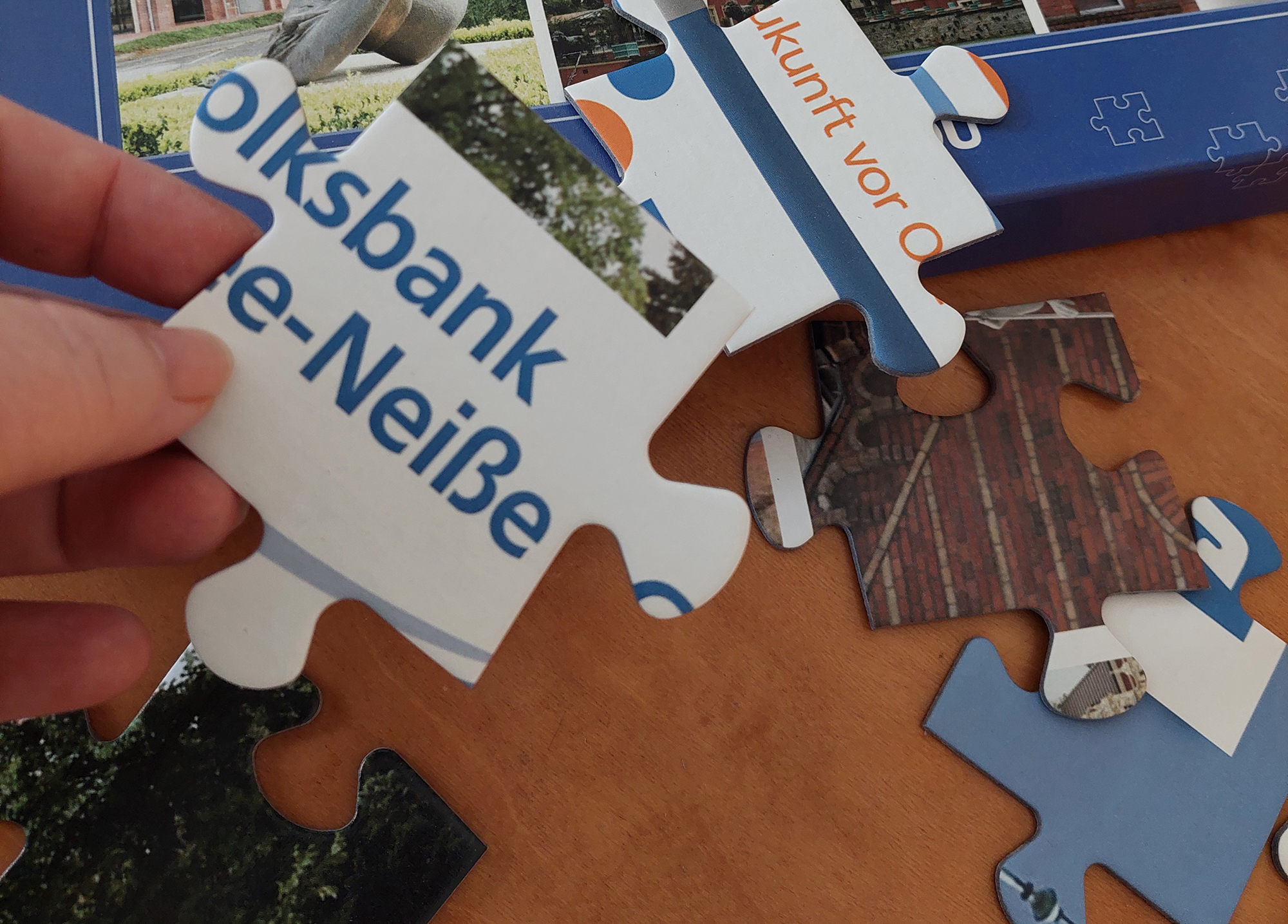 In der Hand wird ein Puzzle-Teil gehalten und weitere liegen auf dem Tisch