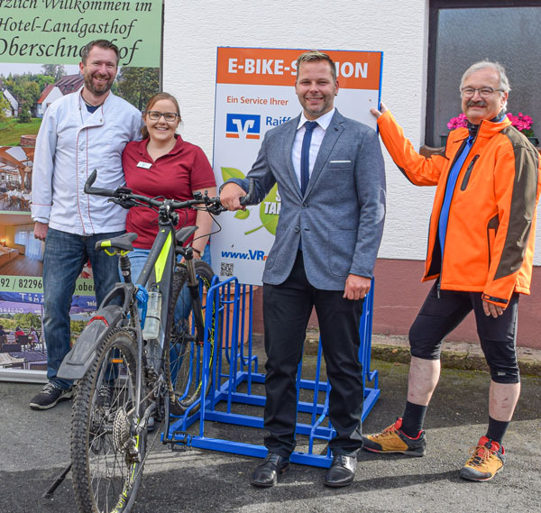 Freude auf allen Seiten: Glücklich nehmen Geschäftsstellenleiter Torsten Roth (Mitte) und Roland Bauer, Bürgermeister von Dammbach (rechts) sowie die Pächter vom Oberschnorrhof Pavel und Anna-Marietta Matousek (links) die E-Bike-Station in Betrieb.