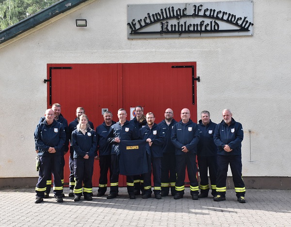 Mitglieder der Freiwilligen Feuerwehr Kuhlenfeld stehen mit ihren neuen Softshelljacken vor dem Feuerwehrgebäude